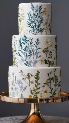 a three tiered cake decorated with flowers and leaves on a gold plated stand