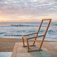 a wooden chair sitting on top of a tiled floor next to the ocean at sunset