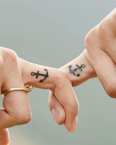 two people holding hands with tattoos on their fingers and the other hand is pointing to each other