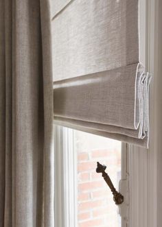 an open window with roman blinds in the corner and a key hanging on the curtain rod