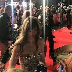 a woman in a strapless dress is looking at her cell phone while standing on the red carpet