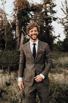 a man wearing a suit and tie standing in front of some trees with his hands in his pockets