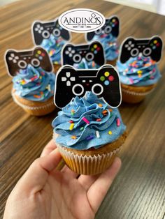 cupcakes with blue frosting and video game controllers on top are being held by a person