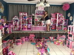 a woman standing on top of a table filled with lots of barbie dolls and furniture