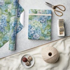 a table topped with blue wrapping paper next to scissors and other crafting supplies on top of a white surface