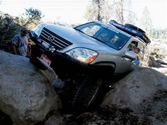 a car that is sitting on top of some rocks in the dirt with another person standing next to it