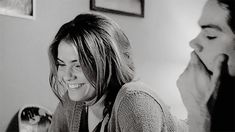 a black and white photo of a woman smiling with another woman looking at her phone