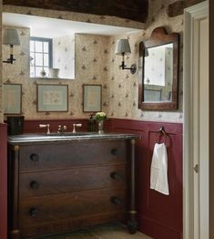 a bathroom with red walls and wallpaper has an antique dresser in the corner, along with two mirrors on the wall