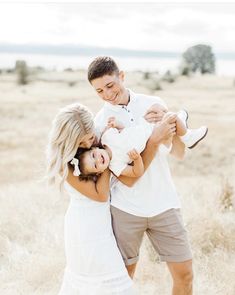 a man and woman holding a baby in the middle of a field