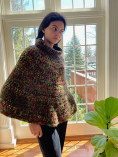 a woman standing in front of a window wearing a multicolored ponchle