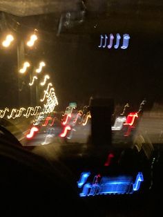 blurry photograph of cars driving at night with colorful lights on the street and trees in the background