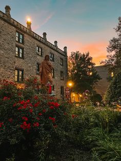 there is a statue in front of a building with red flowers growing on the ground