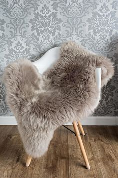 a white chair with a fur seat cover on it in front of a wallpapered background