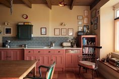 an old fashioned kitchen with pink cabinets and green tile backsplash, wooden dining table