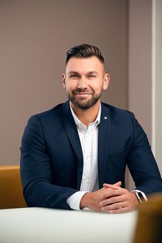 a man sitting at a table with his arms crossed and looking into the camera while smiling