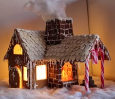 a lighted gingerbread house with candy canes on the roof and chimney in the snow