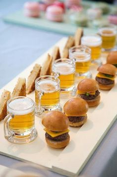 there are many small sandwiches and glasses of beer on the long serving tray with bread