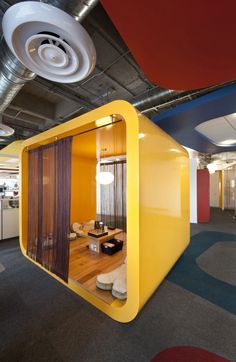 an office cubicle with yellow and red walls, carpeted flooring and round lights