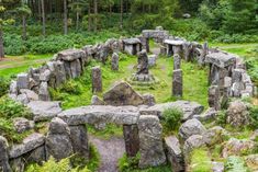 an old stone structure in the middle of a forest filled with green grass and rocks