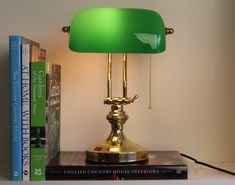 a green lamp sitting on top of a book shelf next to a stack of books