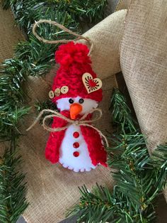 a red and white snowman ornament hanging from a christmas tree on burlap