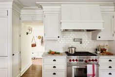 a kitchen with white cabinets and stainless steel stove top oven in the center, surrounded by wooden flooring