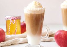 two glasses filled with liquid and topped with whipped cream next to apples on a table