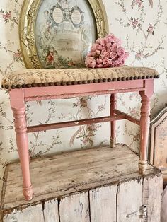 an old wooden bench with pink flowers on it next to a wallpapered wall