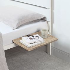 a coffee cup and eyeglasses are on a small table next to a bed