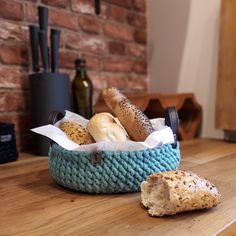 bread and rolls in a blue basket on a wooden table next to a brick wall