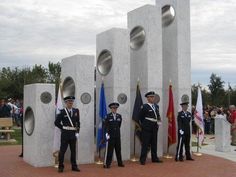 three men in uniform standing next to each other near flags and cement pillars with speakers on them