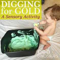 a baby sitting on the floor playing with a green cake in a black container that says digging for gold