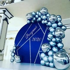 a blue table topped with lots of silver balls and balloons in front of a clock