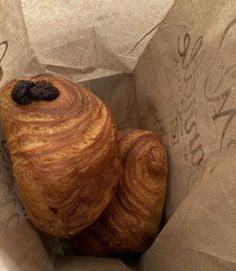 two croissants in a brown paper bag with writing on the side and one has a black bean