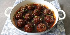 meatballs with sauce and green onions in a white bowl on a blue napkin next to a fork