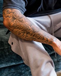 a man with a tattoo on his arm sitting on a couch holding a cell phone