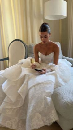 a woman in a white wedding dress sitting on a bed looking at her cell phone