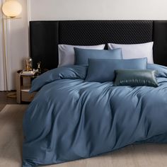 a bed with blue sheets and pillows on top of it in a bedroom next to a night stand