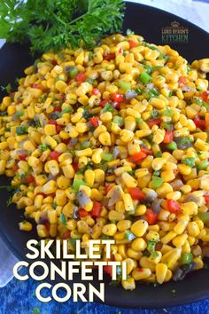 a black plate topped with corn and veggies on top of a blue cloth