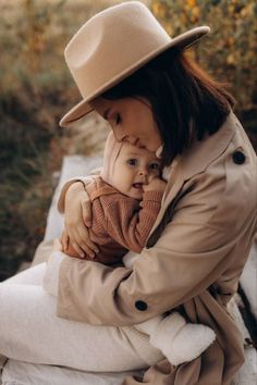 a woman holding a baby in her lap while wearing a brown hat and trench coat