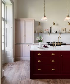 a kitchen with white and red cabinets, wood flooring and two lights hanging from the ceiling