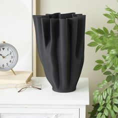 a black vase sitting on top of a white table next to a clock and potted plant