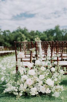 an arrangement of white flowers and greenery sits in front of rows of wooden chairs