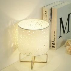 a white lamp sitting on top of a table next to a book and some flowers