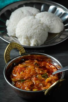 some food is in a metal bowl and on a plate with spoons next to it