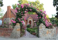 a painting of a house with pink flowers on the front gate and brick fence surrounding it