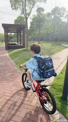 a young boy is riding his bike in the park with a backpack on it's back