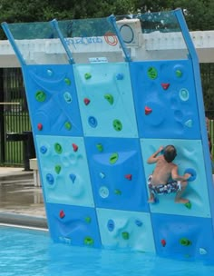 a young boy climbing up the side of a water slide in a swimming pool with no shirt on