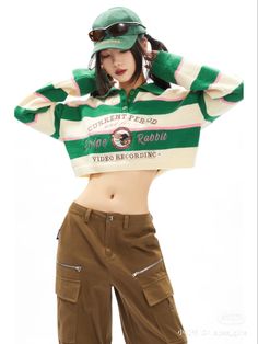 a woman in green and white striped shirt posing with her arms behind her head while wearing brown pants