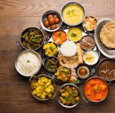 an array of different types of food in metal bowls on a wooden table with utensils